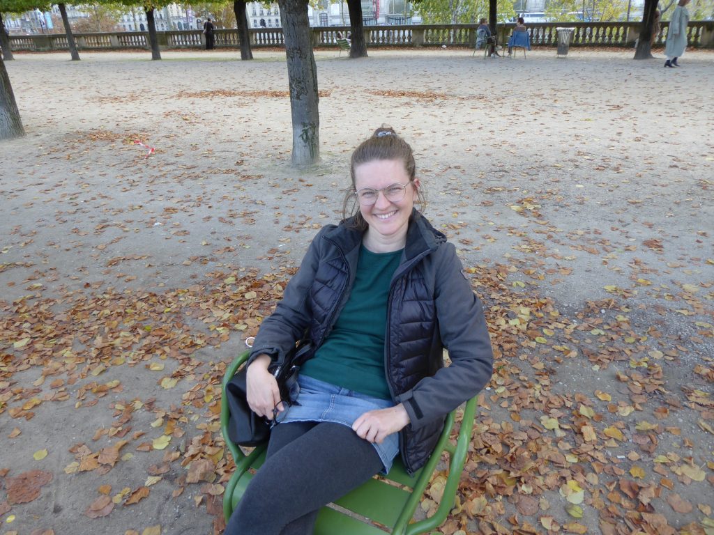 Kathrin Lang sitzt auf einem Stuhl in einem Park.